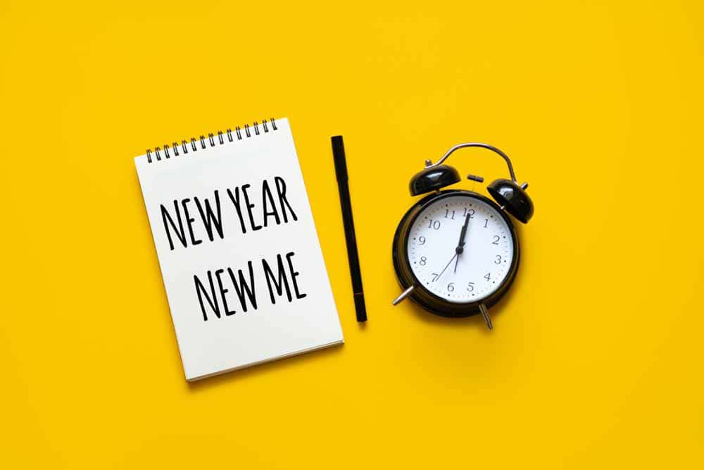 notepad with "New Year - New Me" written on it and an alarm clock