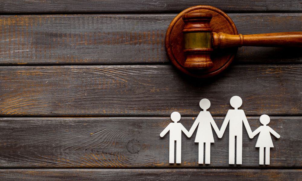 paper doll family on wood table next to a gavel